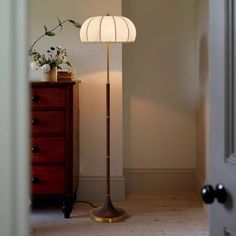 a floor lamp with a white shade on it next to a dresser and chest of drawers