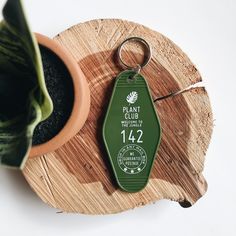 a green keychain sitting on top of a piece of wood next to a potted plant