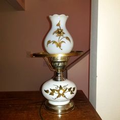 a white vase sitting on top of a wooden table next to a light fixture with gold trim