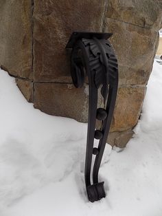 a black metal object sitting in the snow next to a stone wall and tree branch