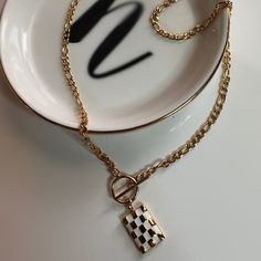 This necklace is made with a classy 18" figaro chain, a toggle clasp to wear in the front, and finished with a checkered pendant. Care instructions: To prolong the lifetime of your item, avoid direct and prolonged contact with harsh chemicals, chlorinated pools, perfumes and lotions. Your jewelry can be cleaned with lukewarm water and a small amount of mild soap. Let it soak for 3-5 minutes and dry with a soft cloth. If you feel the need to deep clean, you can use a soft (preferable baby soft) t Trendy Gold Plated Charm Necklace For Gift, Trendy Gold Charm Necklaces, Trendy Pendant Chain Necklace, Trendy Everyday Pendant Chain Necklace, Trendy Gold-tone Charm Necklace As Gift, Trendy Gold-plated Pendant Chain Necklace, Trendy Gold Rectangular Pendant Jewelry, Trendy Gold Plated Pendant Chain Necklace, Vintage White Chain Necklace For Gift