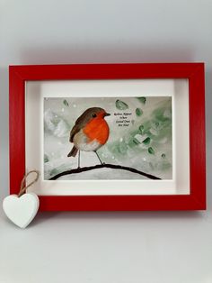 a small red and white bird sitting on top of a branch next to a heart