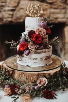 a three tiered cake with red flowers and greenery sits on top of a tree stump