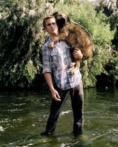 a man holding a dog in his arms while standing on the edge of a river