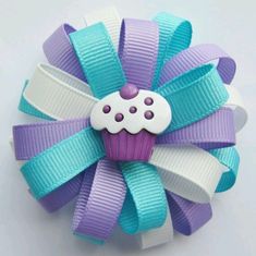 a purple and blue hair bow with a cupcake on the top, sitting on a white surface