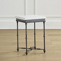 an end table with a white cushion on top and black legs, in front of a white wall