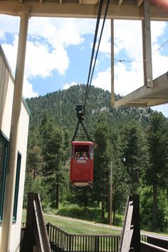 a red cable car going up the side of a mountain with trees in the background