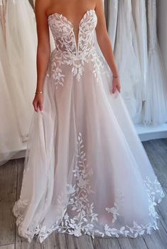 a woman in a wedding dress standing next to some dresses on display at a bridal shop