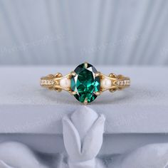 a ring with a green stone surrounded by white pearls and gold plating on top