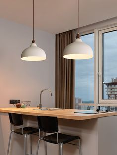 two lights hanging over a kitchen island with bar stools in front of the window