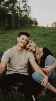 a young man and woman sitting in the grass smiling at the camera with their arms around each other