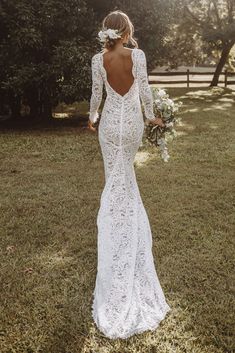 a woman in a wedding dress is walking through the grass with her back to the camera