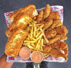 fried chicken, french fries and dipping sauces on a paper wrapper with someone's feet