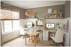 a home office with two computer desks and shelves on the wall above them,