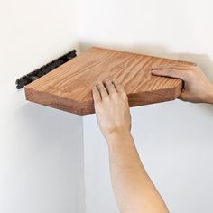 a person with their hand on the edge of a wooden shelf that is being held up