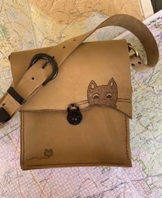 Adorable Cat and mouse on light brown leather purse. This bag is 9x8 with a 16 inch strap. The Phone pouch and the card pocket are plaid print on leather.  My bags are inspired by the Swiss Army Knife, made to last a lifetime with useful features. I like distressed leather and rugged edges. I feel it gives my pieces their own personality. All items are 100% made by me, from design to all the hand sewing (saddle stitch) .Each bag takes about 8 hours of work time. Cat Design Pouch Shoulder Bag For Travel, Travel Pouch Shoulder Bag With Cat Design, Daily Use Crossbody Bag With Cat Design, Beige Bag With Cat Design For Everyday Use, Beige Cat Design Bag For Everyday Use, Beige Rectangular Bag With Cat Design, Travel Shoulder Bag With Cat Design, Everyday Beige Bag With Cat Design, Cat Design Crossbody Travel Bag