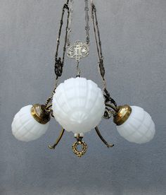 a chandelier with three white glass shades hanging from it's arms and two brass chains