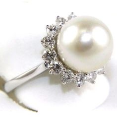 a white pearl and diamond ring on a white surface with the center surrounded by small diamonds