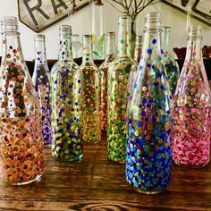 there are many different colored glass bottles on the table and one is filled with confetti