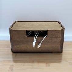 a wooden box with wires in it on a wood floor next to a white wall