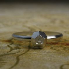 a silver ring with an initial on it sitting on a tablecloth covered floor in front of a wall