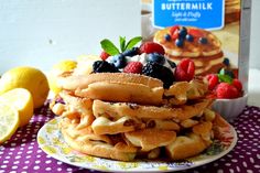 a stack of waffles topped with berries and blueberries next to a carton of buttermilk