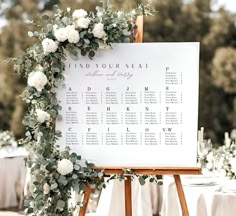 a seating chart with white flowers and greenery is displayed on an easel at a wedding reception