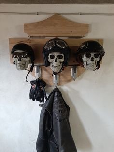 three skulls wearing helmets and gloves hang on a coat rack with leather gloves hanging from it