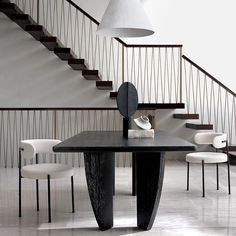 a black table and white chairs in front of a stair case with a mirror on it