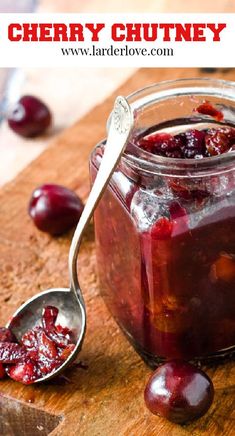 a jar filled with cherries sitting on top of a wooden cutting board next to a spoon