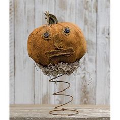 a pumpkin with eyes and mouth sitting on top of a metal wire stand in front of a wooden wall