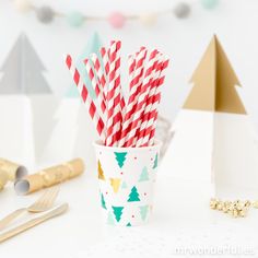 red and white striped paper straws in a cup on a table next to christmas decorations