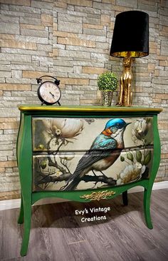 a green dresser with a bird painted on the front and bottom, next to a clock