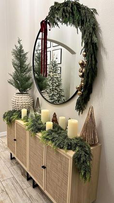 a christmas mantle with candles and greenery on it in front of a round mirror