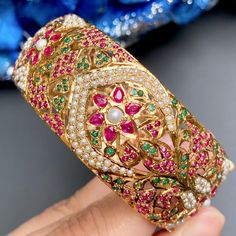 Featuring a broad jadau kada/bangle made on sterling silver with gold plating. It has been intricately studded with ruby like red stones, emerald like green stones and freshwater pearls. The bangle comes openable in size 2inch 5 anna and this design can be customized to your size. Ruby Bangle With Intricate Design, Ruby Temple Jewelry Bracelet With Intricate Design, Temple Style Ruby Bangle Jewelry, Ruby Temple Jewelry Bracelets For Festivals, Intricate Design Ruby Bangle Jewelry, Traditional Ruby Bracelets With Jeweled Detail, Ruby Bangle With Intricate Design For Gift, Intricate Ruby Bangle Jewelry, Traditional Ruby Bangle Bracelets