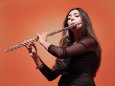 a woman is playing the flute in front of an orange background and she has long dark hair