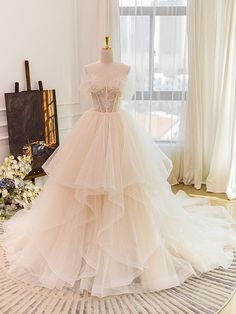 a wedding dress on display in front of a window with white curtains and floral arrangements