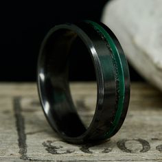 a black and green wedding ring sitting on top of a wooden table