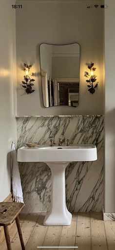 a white sink sitting under a bathroom mirror next to a wooden table and chair in front of it