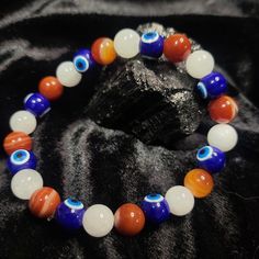 This stylish Mystic 'Merica bracelet features a unique combination of Quartz, Banded Carnelian, and evil eye beads in a patriotic red, white, and blue stretch design. Perfect for anyone looking for a touch of protection and style all in one accessory. Handmade Symbolic White Beaded Bracelet, Handmade White Symbolic Beaded Bracelets, White Evil Eye Bracelet With 8mm Beads As Gift, White Hand-strung Evil Eye Bracelet With Round Beads, White Round Evil Eye Bracelet, Symbolic White Round Bead Bracelets, Symbolic White Bracelets With Round Beads, White Spiritual Evil Eye Bracelet With Colorful Beads, Spiritual White Beaded Bracelets With Evil Eye