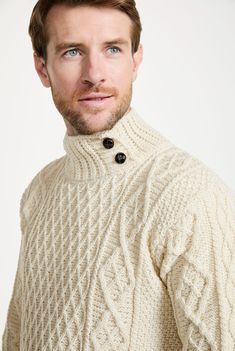 a man wearing a white sweater and black buttoned up shirt is looking at the camera