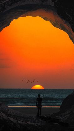 a man standing in the middle of a cave looking out into the ocean at sunset