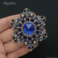 a hand holding a blue and silver brooch