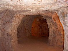 an underground passage in a rock formation with dirt flooring and red paint on the walls