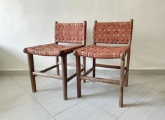 two wooden chairs sitting next to each other on a white tile floor in front of a wall