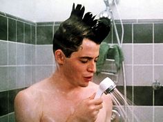 a shirtless man is holding a hair dryer and spraying water on his head