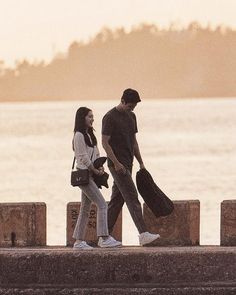 two people are walking along the water with their bags in hand and one is carrying luggage