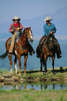 two people riding horses next to a body of water