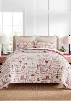 a bed with red and white comforter in a room next to a lamp on a table