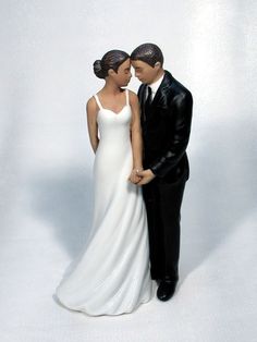 a bride and groom figurine standing next to each other on a white background